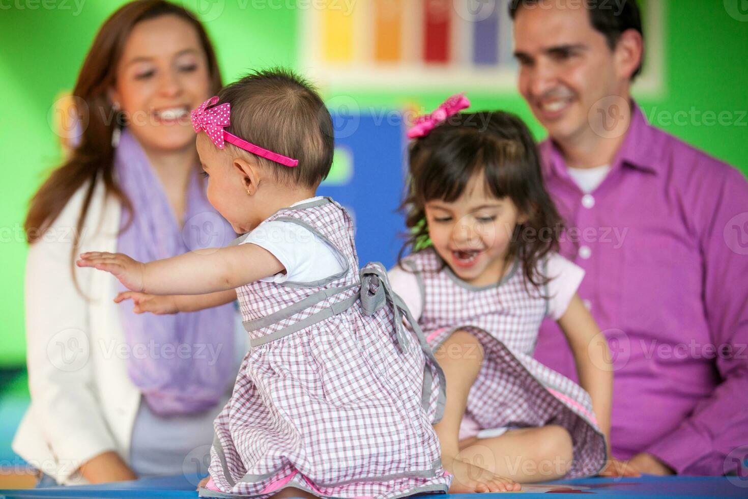 lindo dez meses bebê menina jogando com dela irmã e seus pais em fundo.. cedo estimulação para crianças e crianças conceito. foto