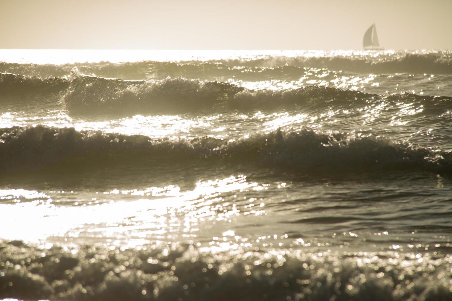 ondas do mar sob o pôr do sol com forma de veleiro no horison foto