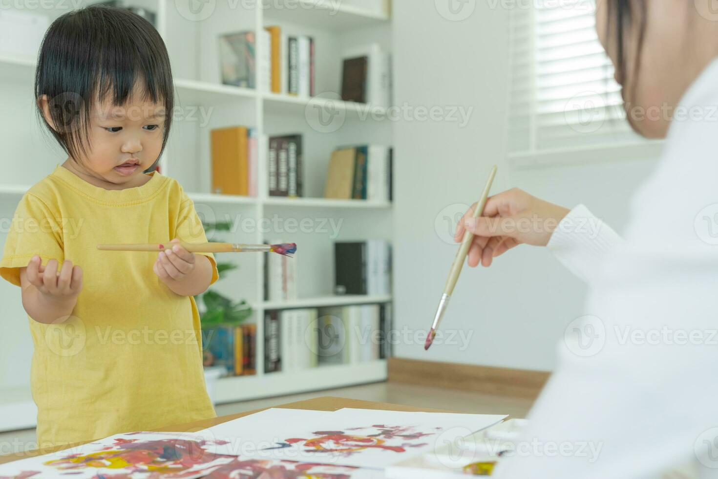 feliz Ásia mãe jogando Aprendendo pintura para pequeno garota. engraçado família é feliz e animado dentro a casa. mãe e filha tendo Diversão gastos Tempo junto. feriado, atividade foto