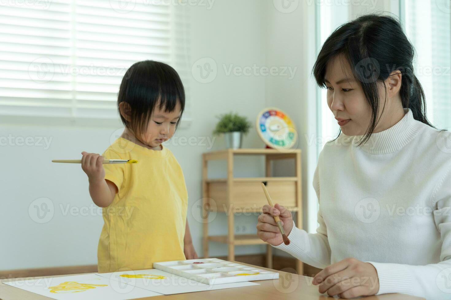 feliz Ásia mãe jogando Aprendendo pintura para pequeno garota. engraçado família é feliz e animado dentro a casa. mãe e filha tendo Diversão gastos Tempo junto. feriado, atividade foto