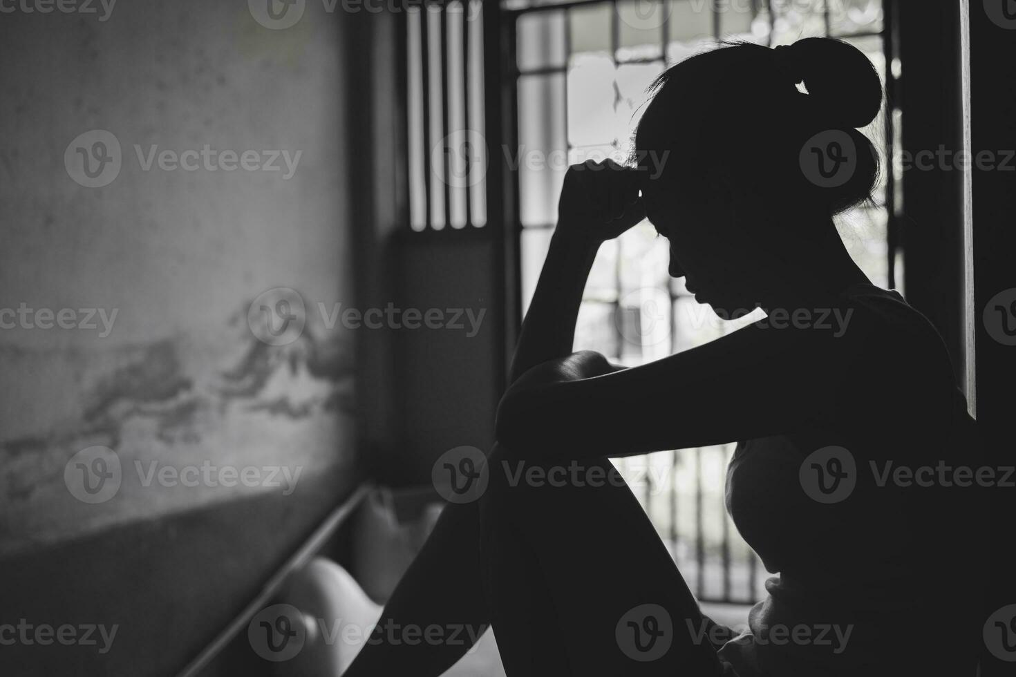 silhueta do depressivo jovem mulher perto janela às lar, fechar-se dentro a Sombrio sala. doméstico violência, violência contra mulheres negras e branco foto. foto
