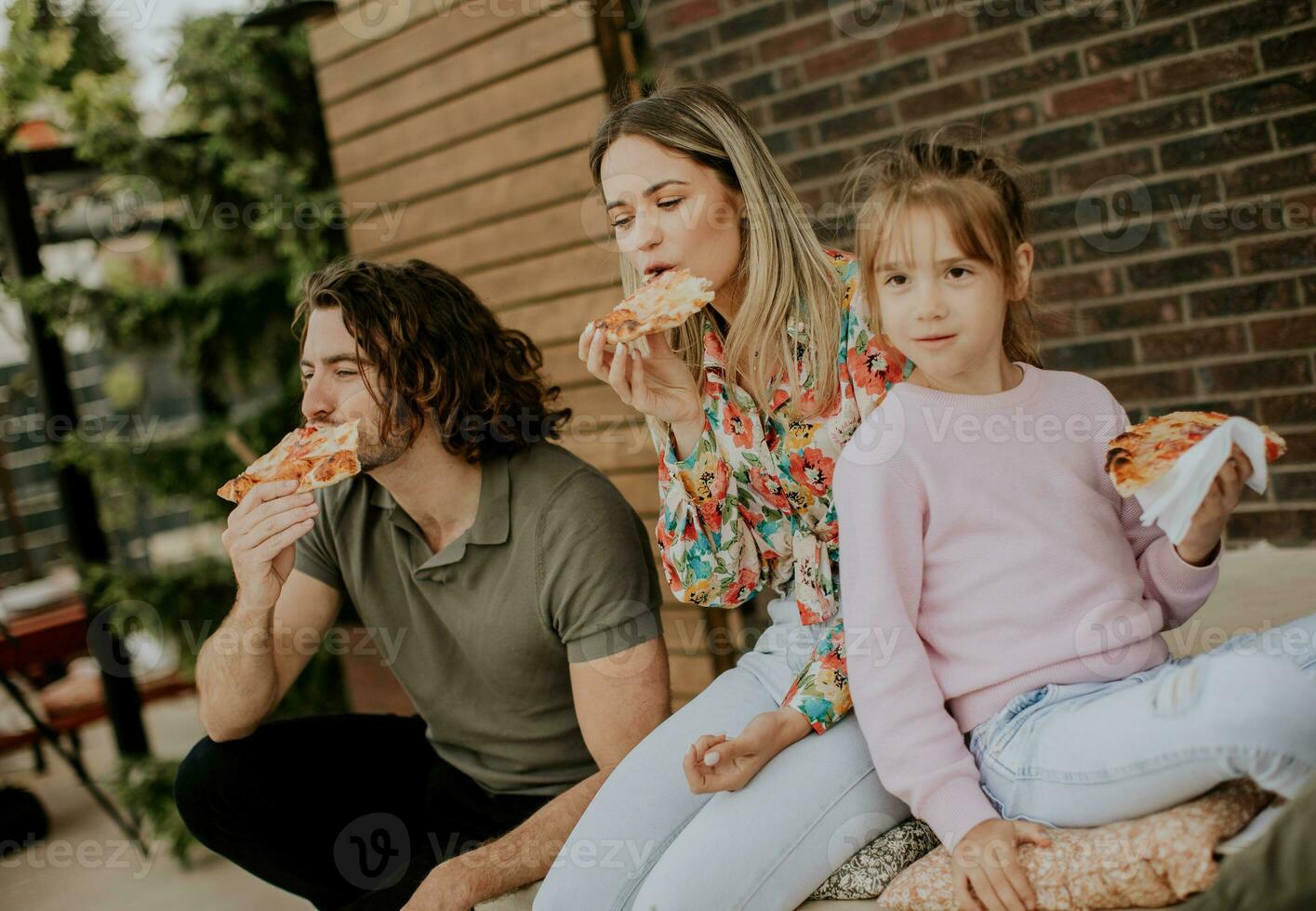 jovem família comendo pizza dentro a casa quintal foto