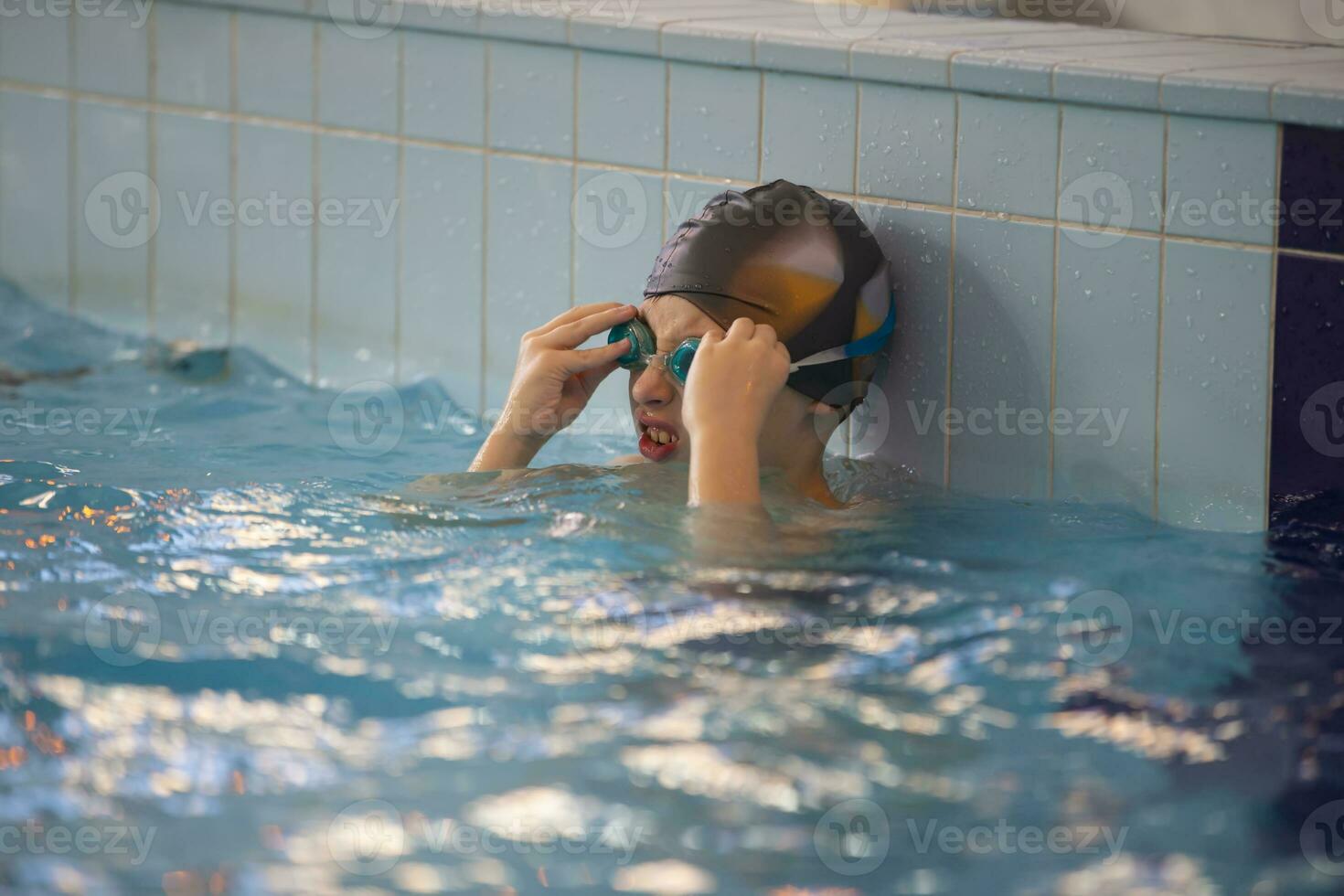 Garoto dentro uma natação boné e natação óculos dentro a piscina. a criança é acionado dentro a natação seção. foto