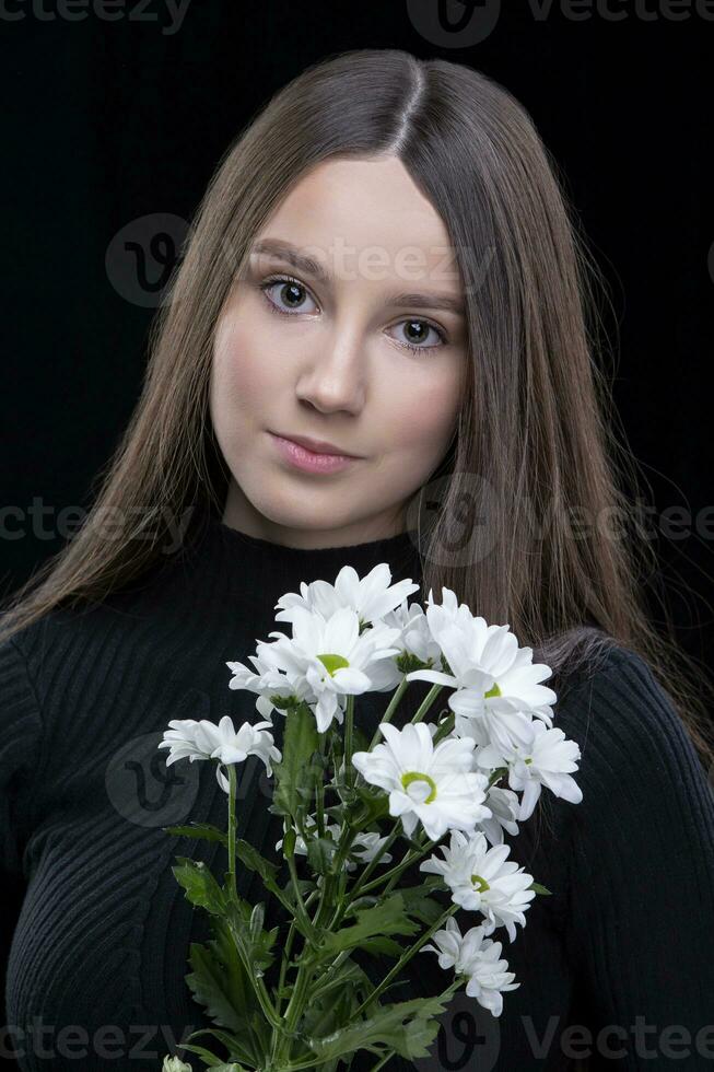 uma lindo jovem menina com natural beleza com grandes suave cabelo detém uma ramalhete do branco crisântemos. foto