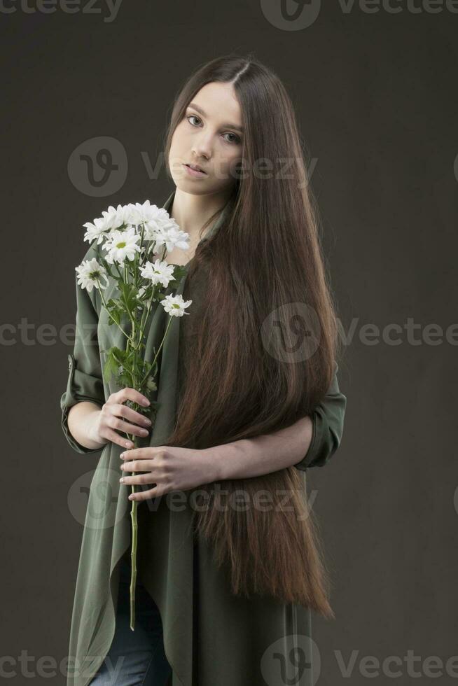 uma lindo jovem menina com natural beleza com grandes suave cabelo detém uma ramalhete do branco crisântemos. foto