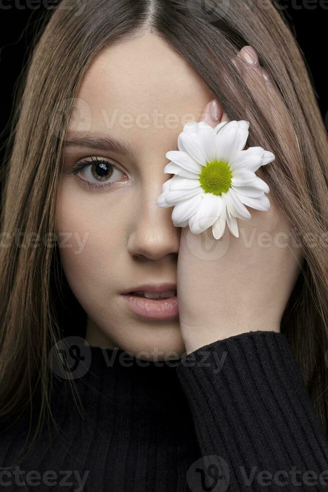 uma lindo menina com natural beleza detém uma branco flor perto dela olho. jovem menina com uma branco crisântemo. foto