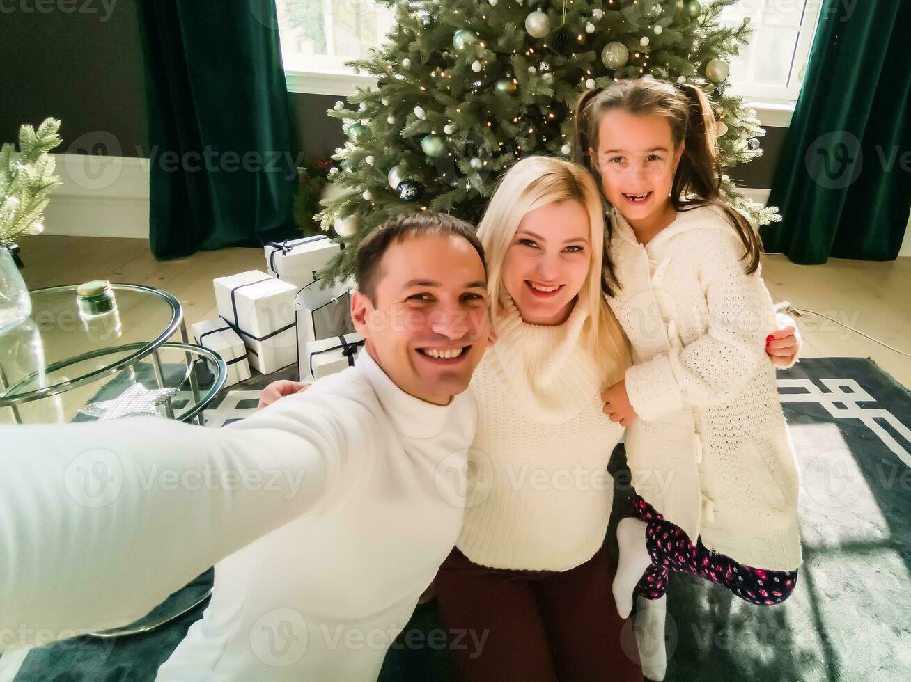 Natal. família. tecnologia. Visão em a Smartphone. pai, mãe e filha olhando às Câmera e sorridente enquanto fazendo selfie foto