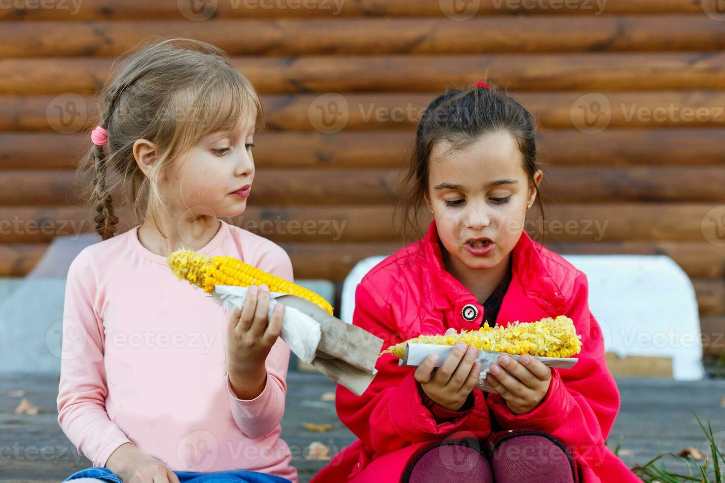 pequeno meninas comendo bagunçado milho em a espiga foto