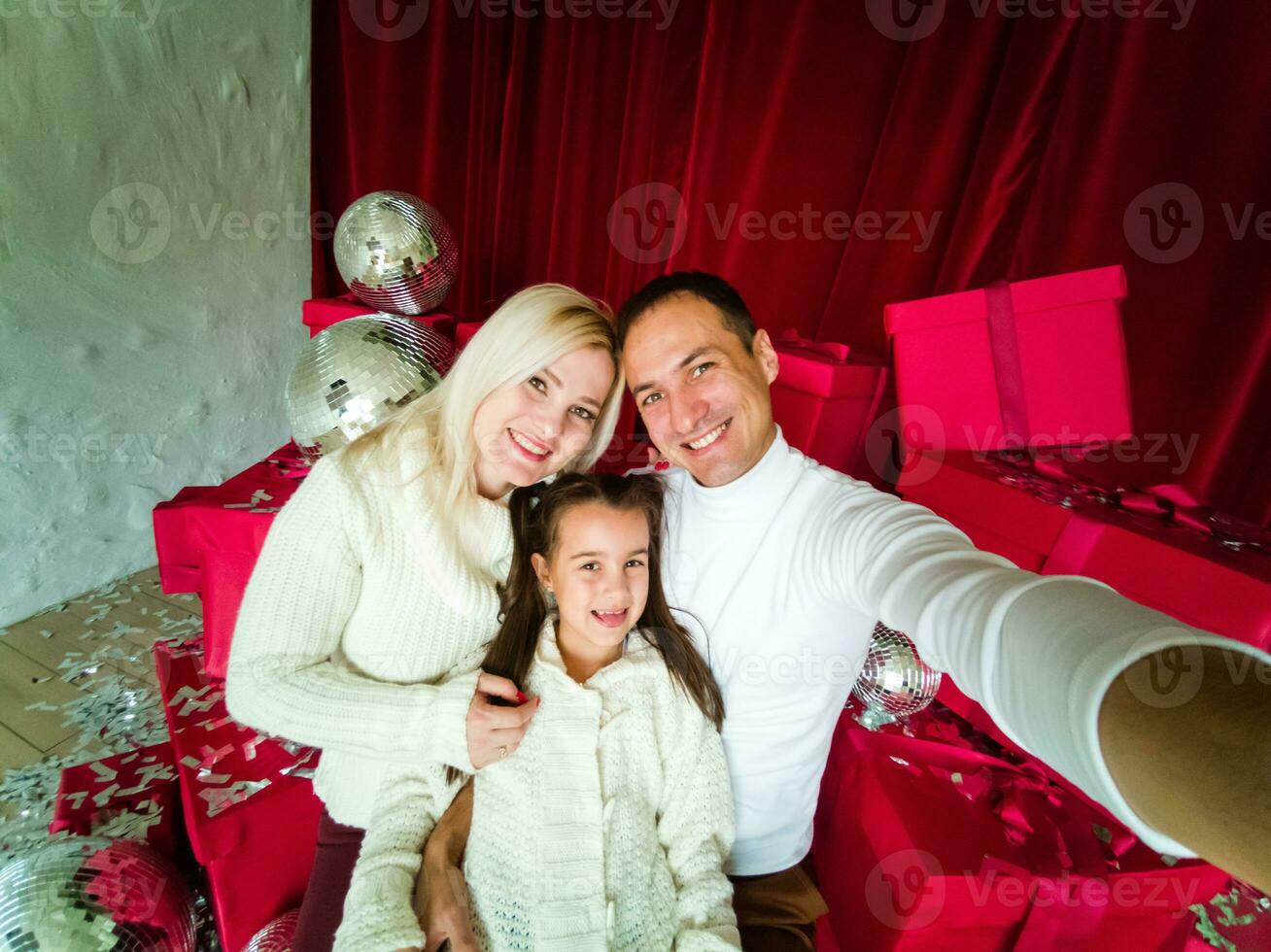 família, feriados, tecnologia e pessoas - sorridente mãe, pai e pequeno menina fazer selfie com Câmera sobre vivo quarto e Natal árvore fundo foto