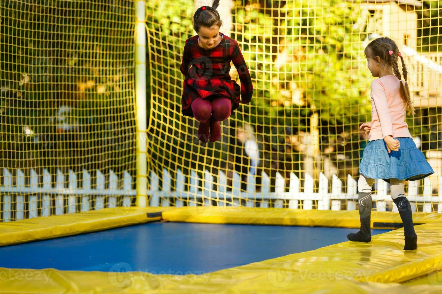 feliz escola menina pulando em trampolim dentro a outono parque foto