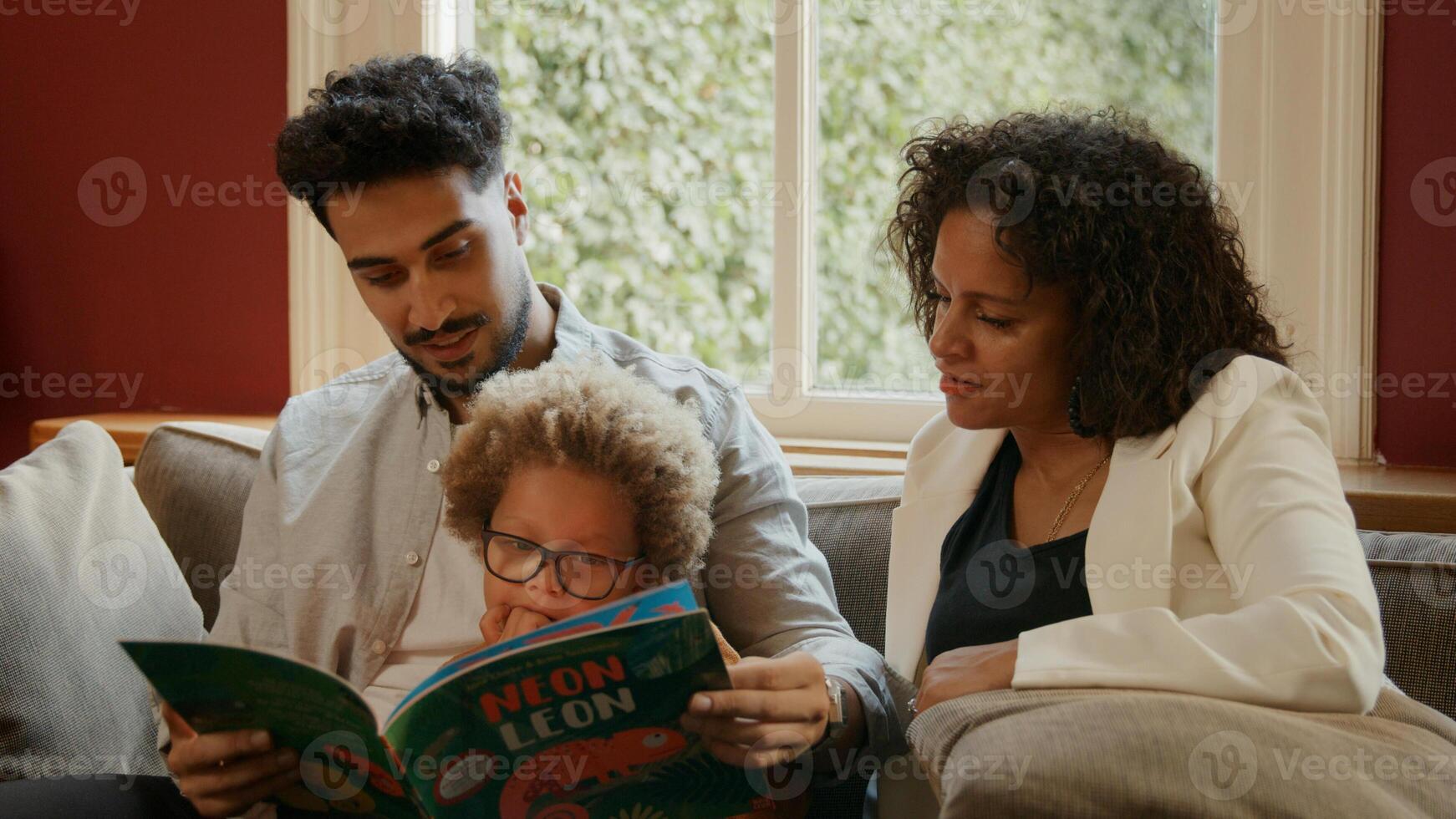 menino lendo livro com os pais em casa foto