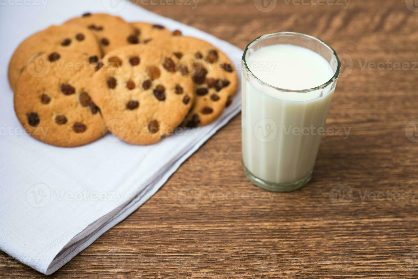 biscoitos perfumados, saborosos e caseiros com passas e um copo de leite fresco na toalha de cozinha branca foto