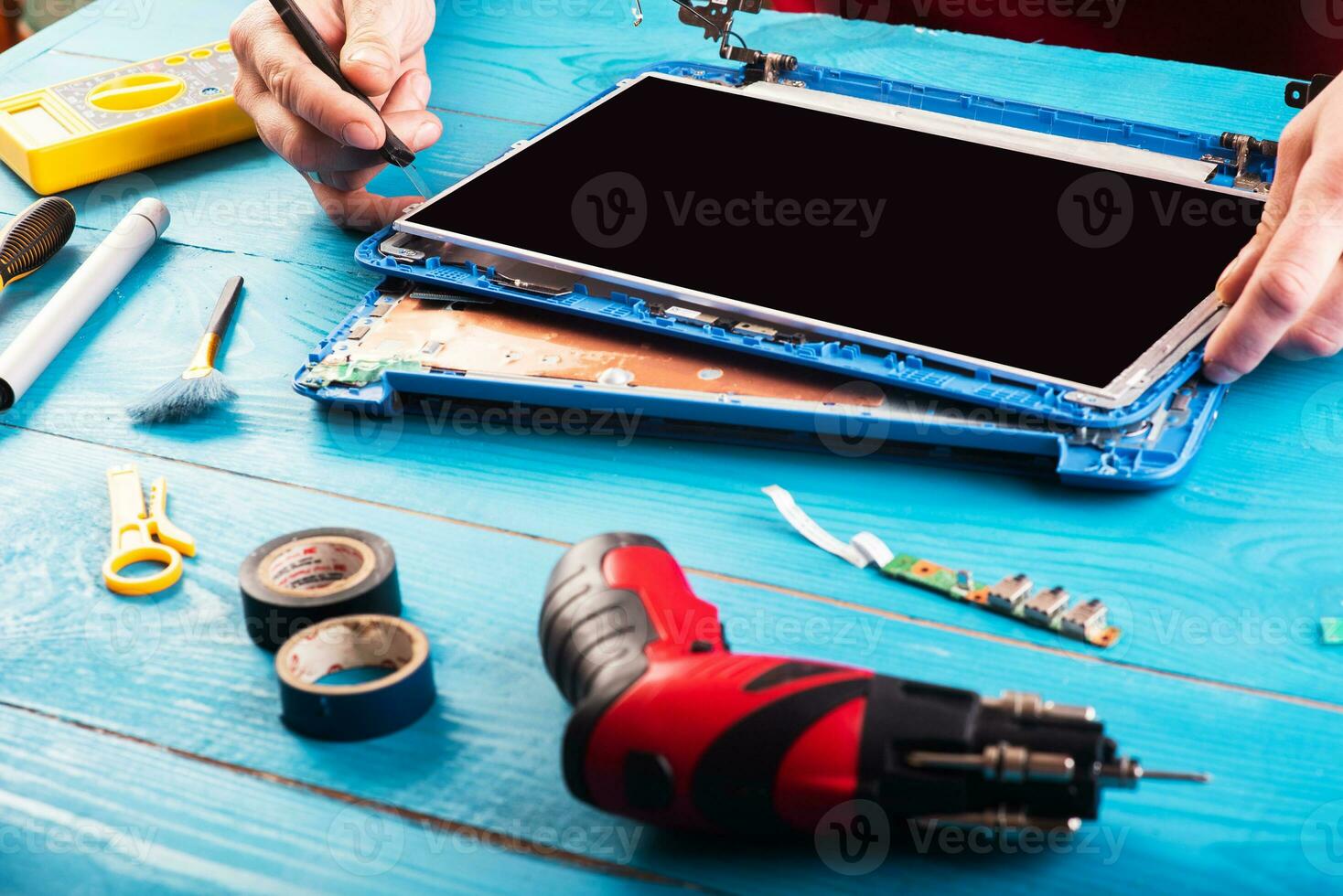 assistente repara laptop com ferramentas e mãos na mesa de madeira azul. vista do topo foto