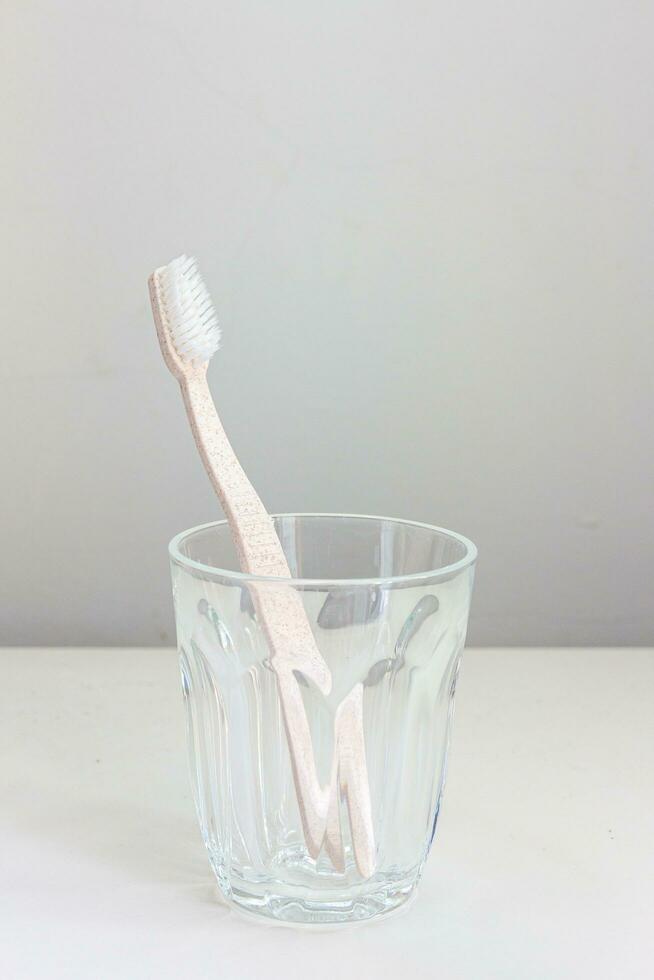 Rosa escova de dente dentro uma vidro colocada em uma branco fundo foto