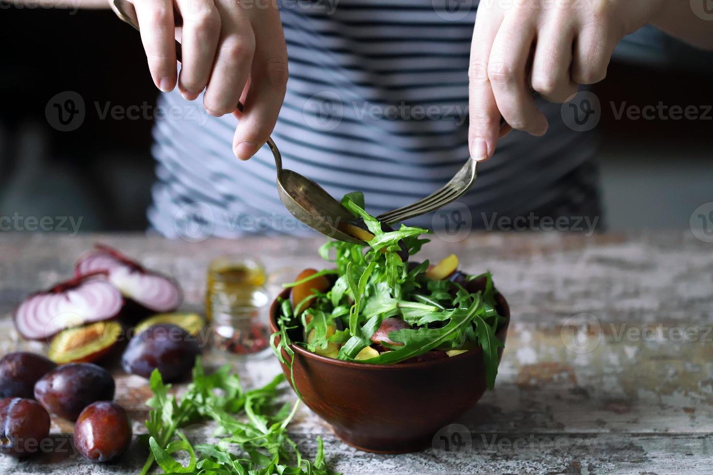 salada saudável misture as mãos masculinas com uma colher e um garfo. salada de ameixa de rúcula. foto