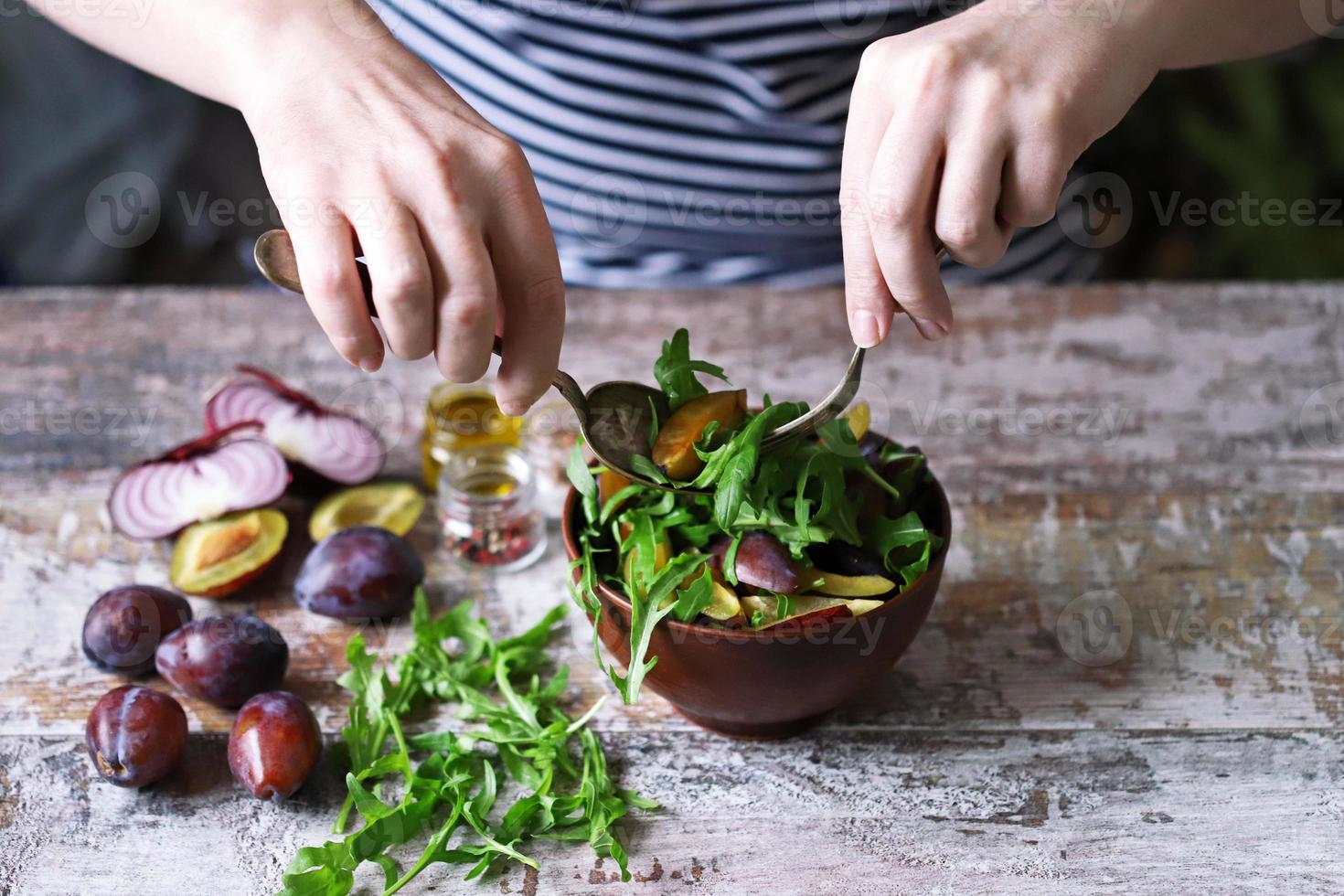 salada saudável misture as mãos masculinas com uma colher e um garfo. salada de ameixa de rúcula. foto