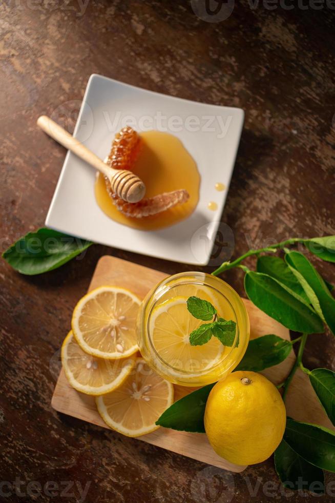suco de limão com mel na mesa de madeira, limões e folhas de sálvia foto