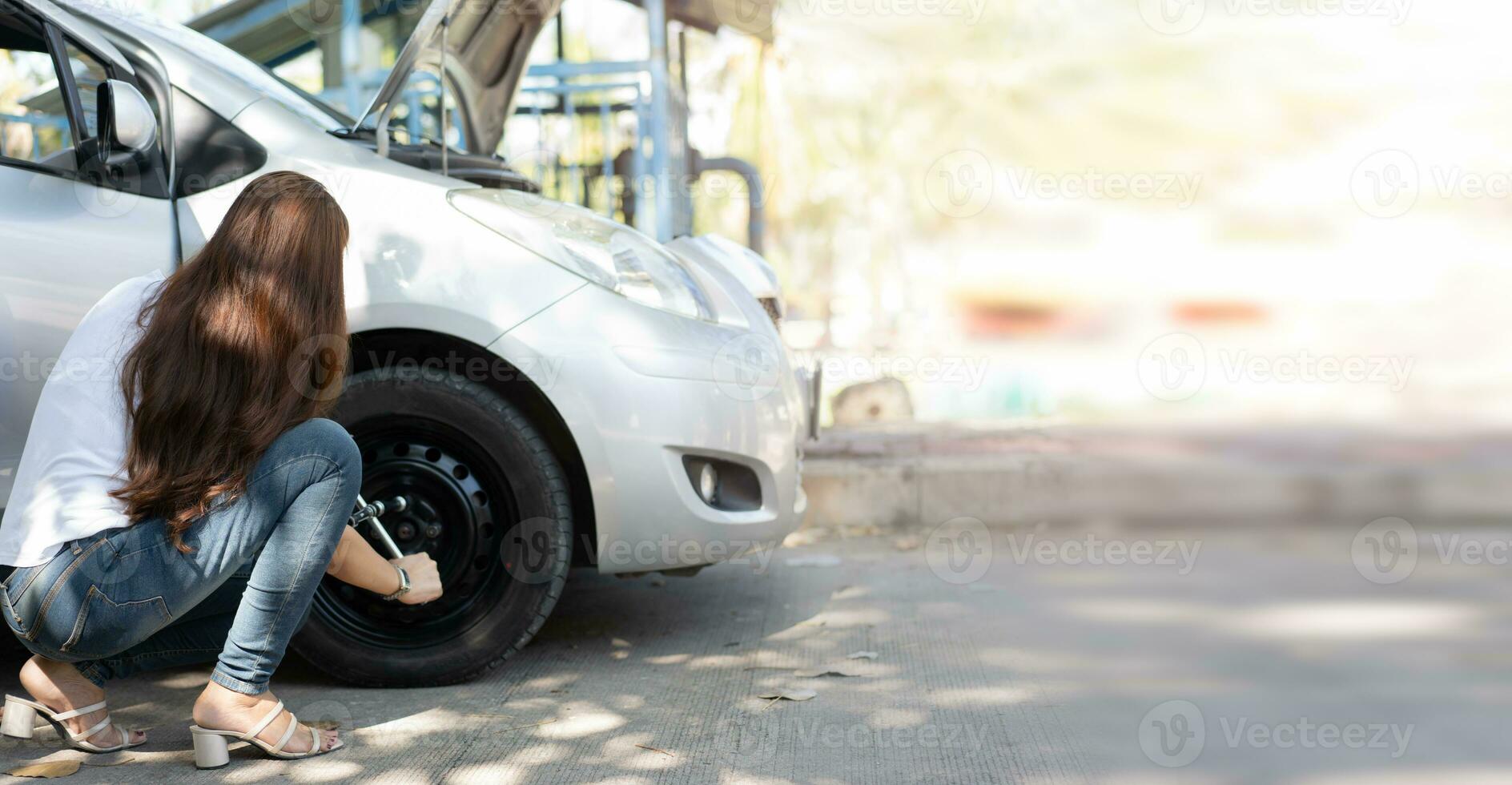 mulher asiática inteligente e atraente levanta seu carro e usa uma chave inglesa para trocar a roda de um carro quebrado, usa ferramentas ou equipamentos, tenta resolver problemas por conta própria, reparação de carros e conceito de seguro foto