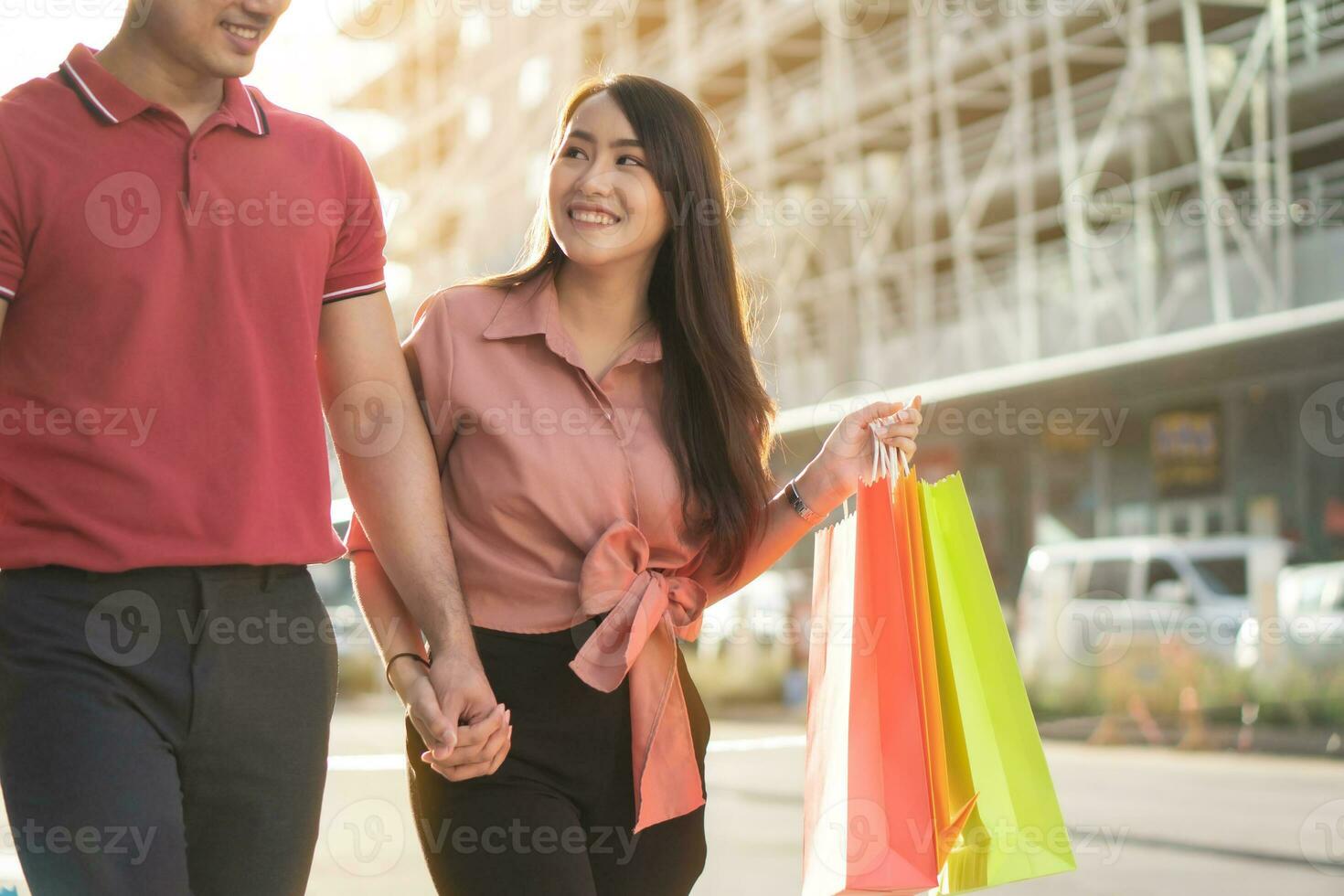 casal jovem feliz de compradores andando na rua comercial em direção e segurando sacolas coloridas na mão. conceito de venda e compras de sexta-feira negra foto