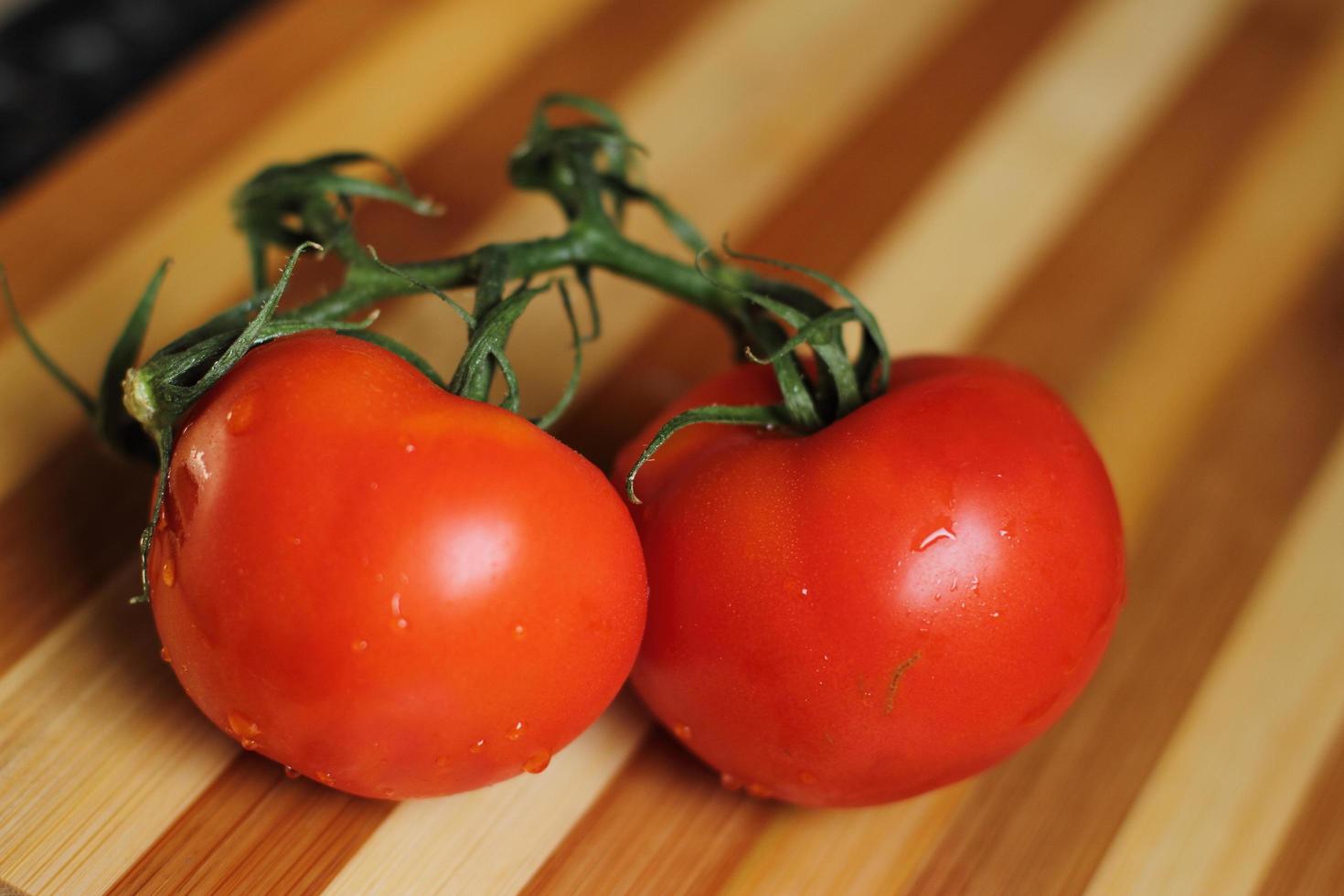 tomates frescos crus com gotas de água na placa de madeira foto