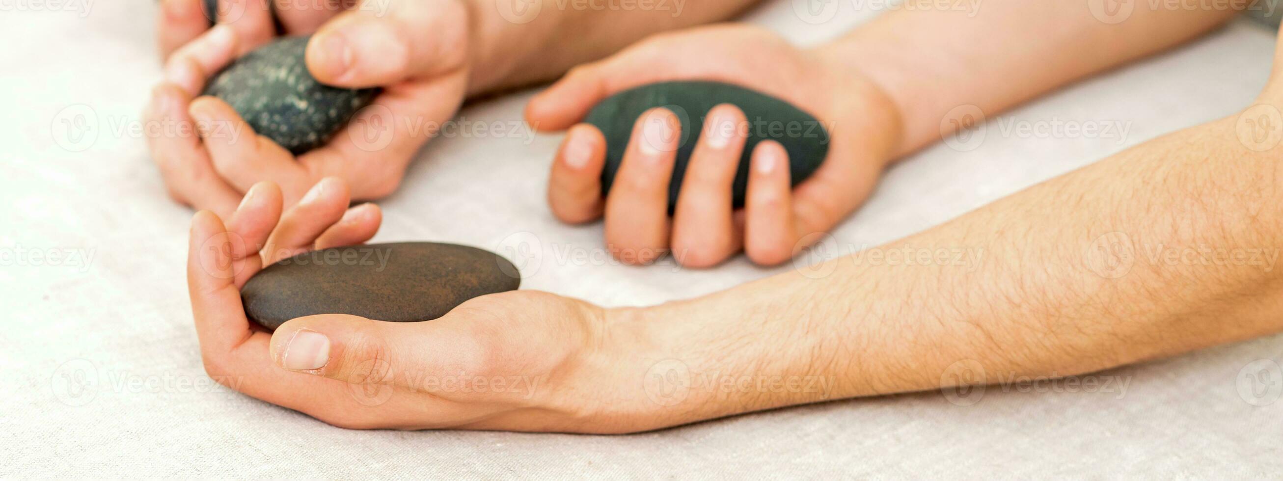 quatro mãos do masculino massagistas segurando spa pedras em branco toalha topo visualizar. pedra massagem conceito. foto