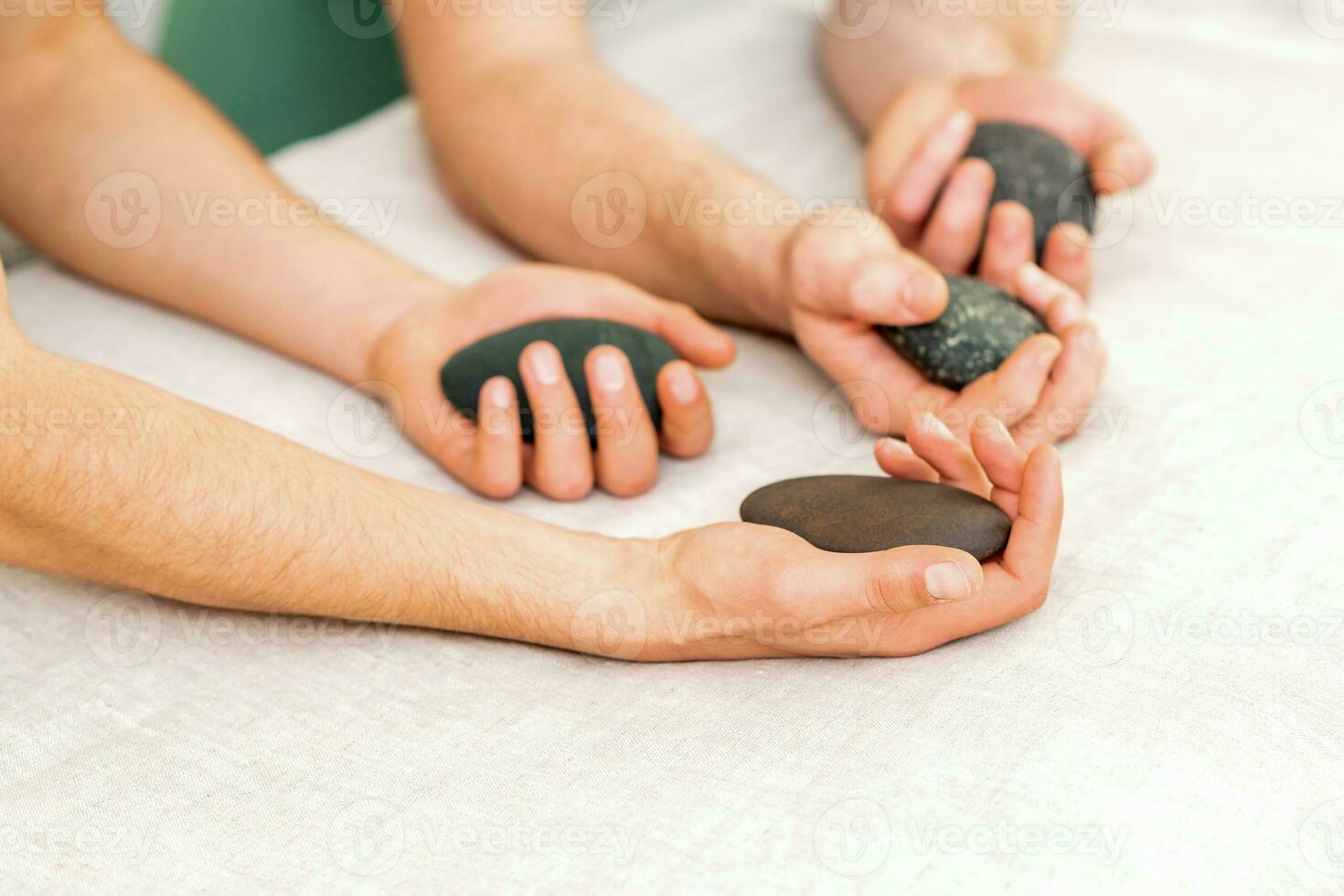 quatro mãos do masculino massagistas segurando spa pedras em branco toalha topo visualizar. pedra massagem conceito. foto