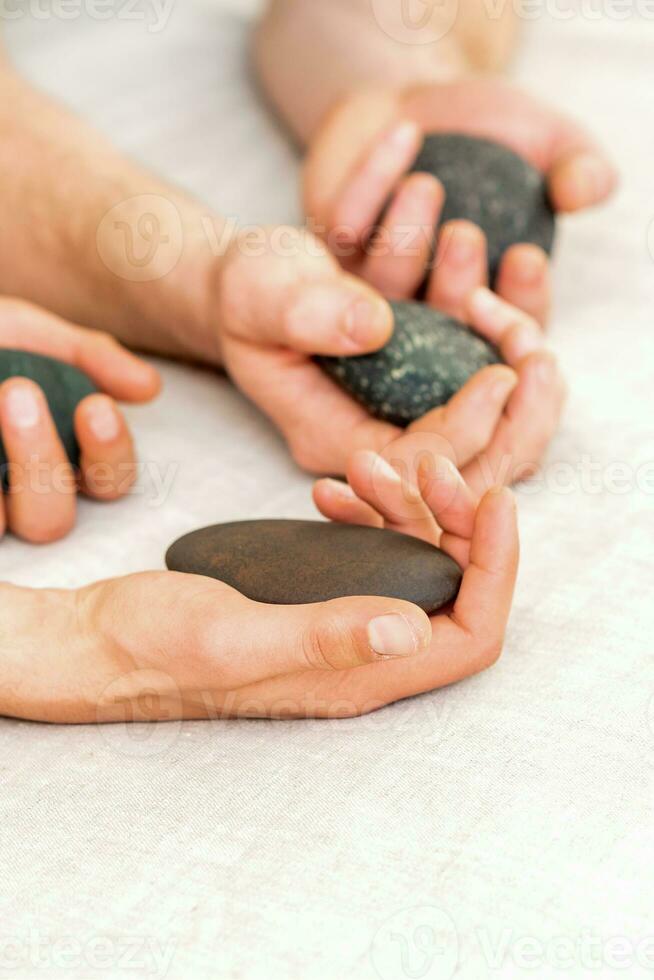 quatro mãos do masculino massagistas segurando spa pedras em branco toalha topo visualizar. pedra massagem conceito. foto