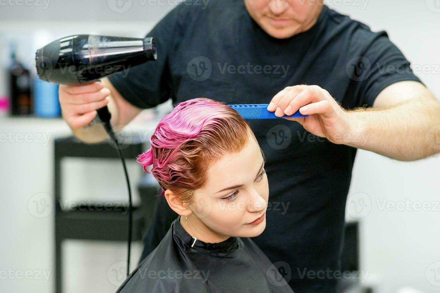 uma cabeleireiro é secagem a Rosa cabelo do a jovem mulher dentro uma beleza salão. foto