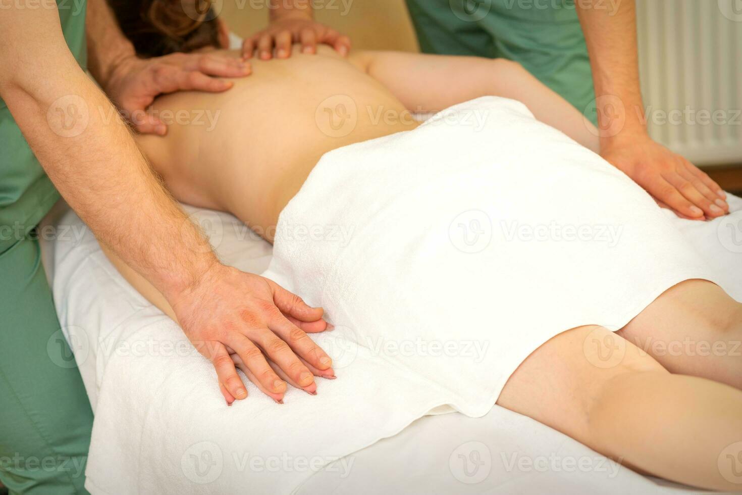costas e mãos Duplo massagem com quatro mãos do dois profissional massageadores para uma jovem caucasiano mulher dentro uma spa salão. foto