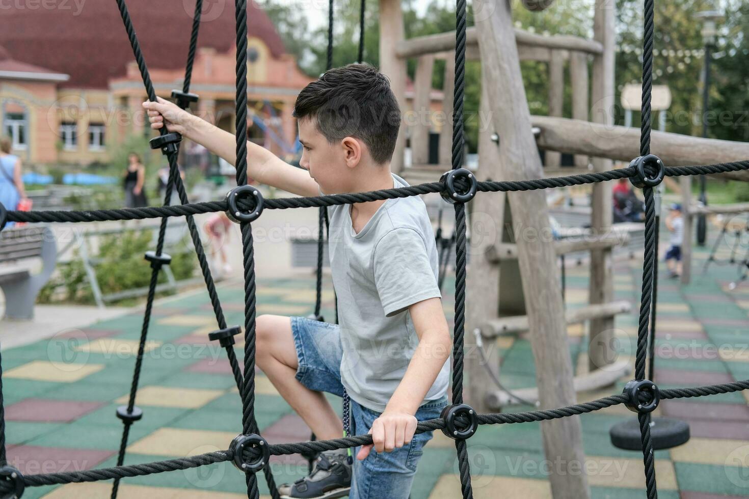 uma Garoto sobe acima a alpino rede em uma Parque infantil foto