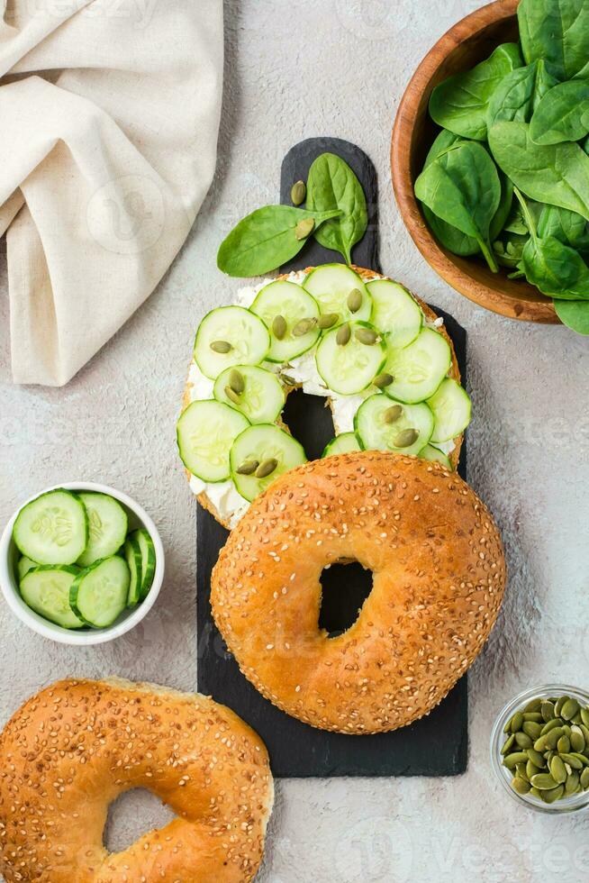 delicioso bagel recheado com queijo feta, pepino e abóbora sementes e espinafre folhas em uma ardósia borda. luz Vitamina saudável lanche. topo e vético Visão foto