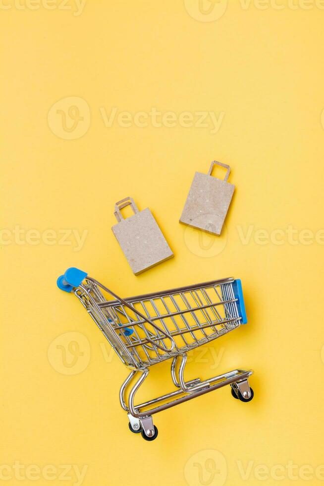 ecológico construir papel bolsas outono dentro uma metal compras carrinho em uma amarelo fundo. Preto sexta-feira, presente vendas. topo e vertical Visão foto