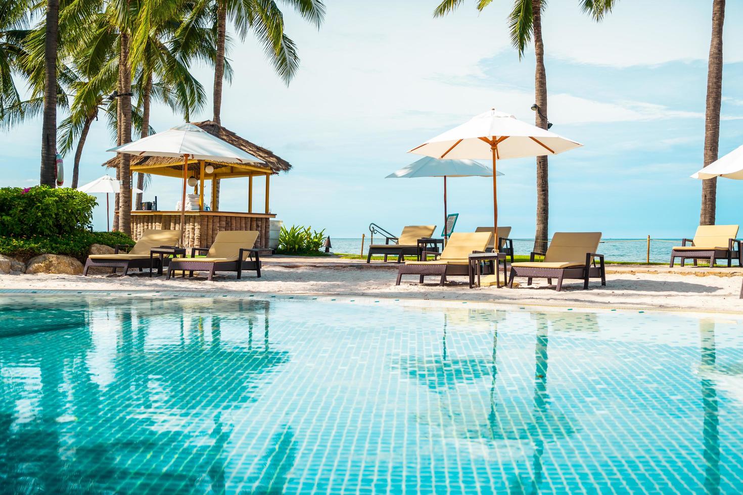 bela praia tropical e mar com guarda-sol e cadeira ao redor da piscina em hotel resort foto