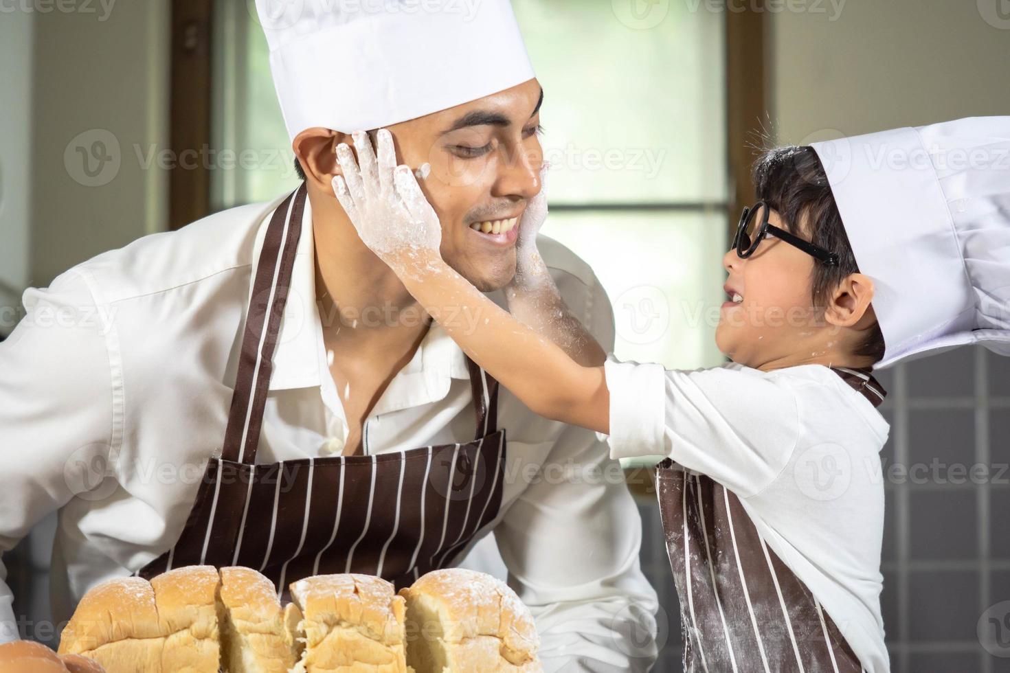 menino asiático usa óculos, provoca o pai cozinhando com farinha branca amassando a massa de pão ensina as crianças a praticar assar ingredientes, pão e ovo em utensílios de mesa na cozinha estilo de vida feliz aprendendo vida com a família foto