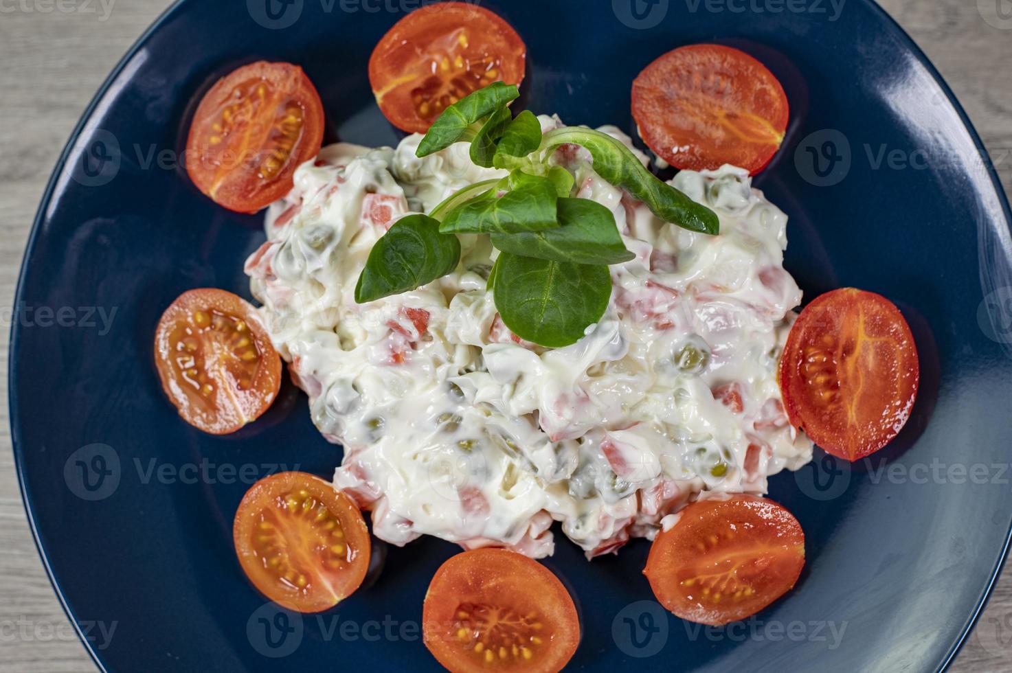 salada russa em prato azul com tomate cereja em fundo de madeira foto