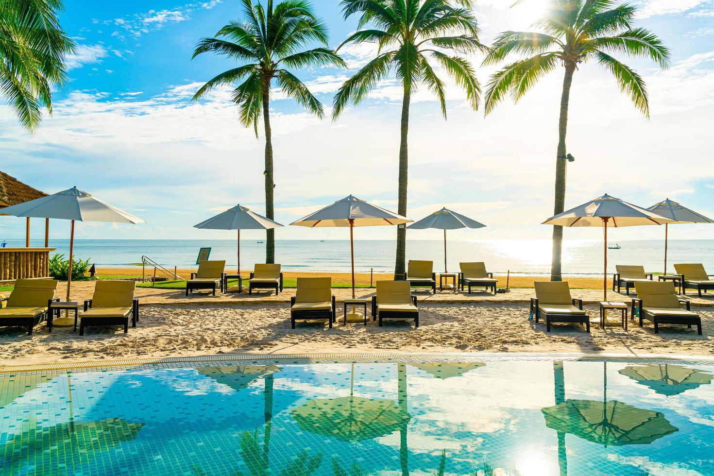 lindo guarda-sol de luxo e cadeira ao redor da piscina externa em hotel e resort com coqueiro no céu azul foto