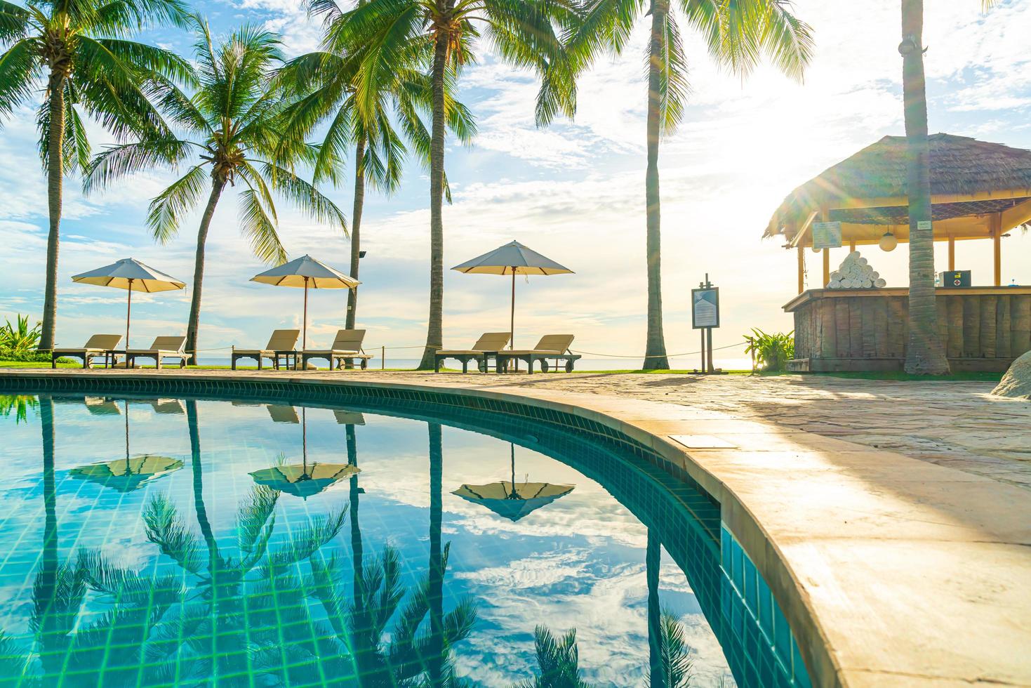 belo guarda-sol de luxo e cadeira ao redor da piscina ao ar livre em hotel e resort com coqueiro no céu do pôr do sol foto