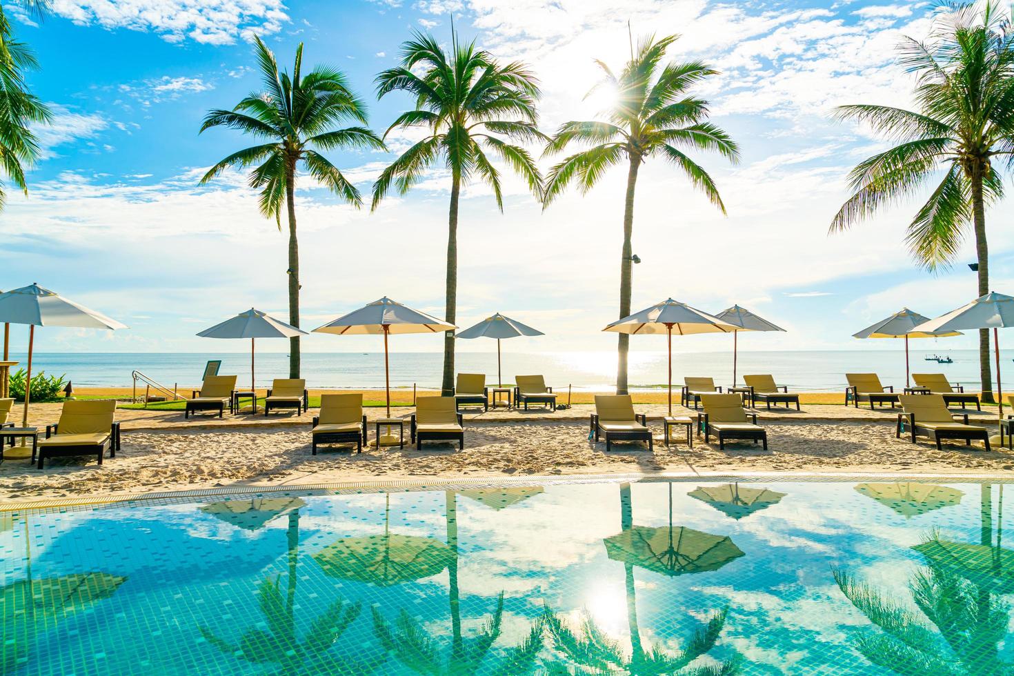 lindo guarda-sol de luxo e cadeira ao redor da piscina externa em hotel e resort com coqueiro no céu azul foto