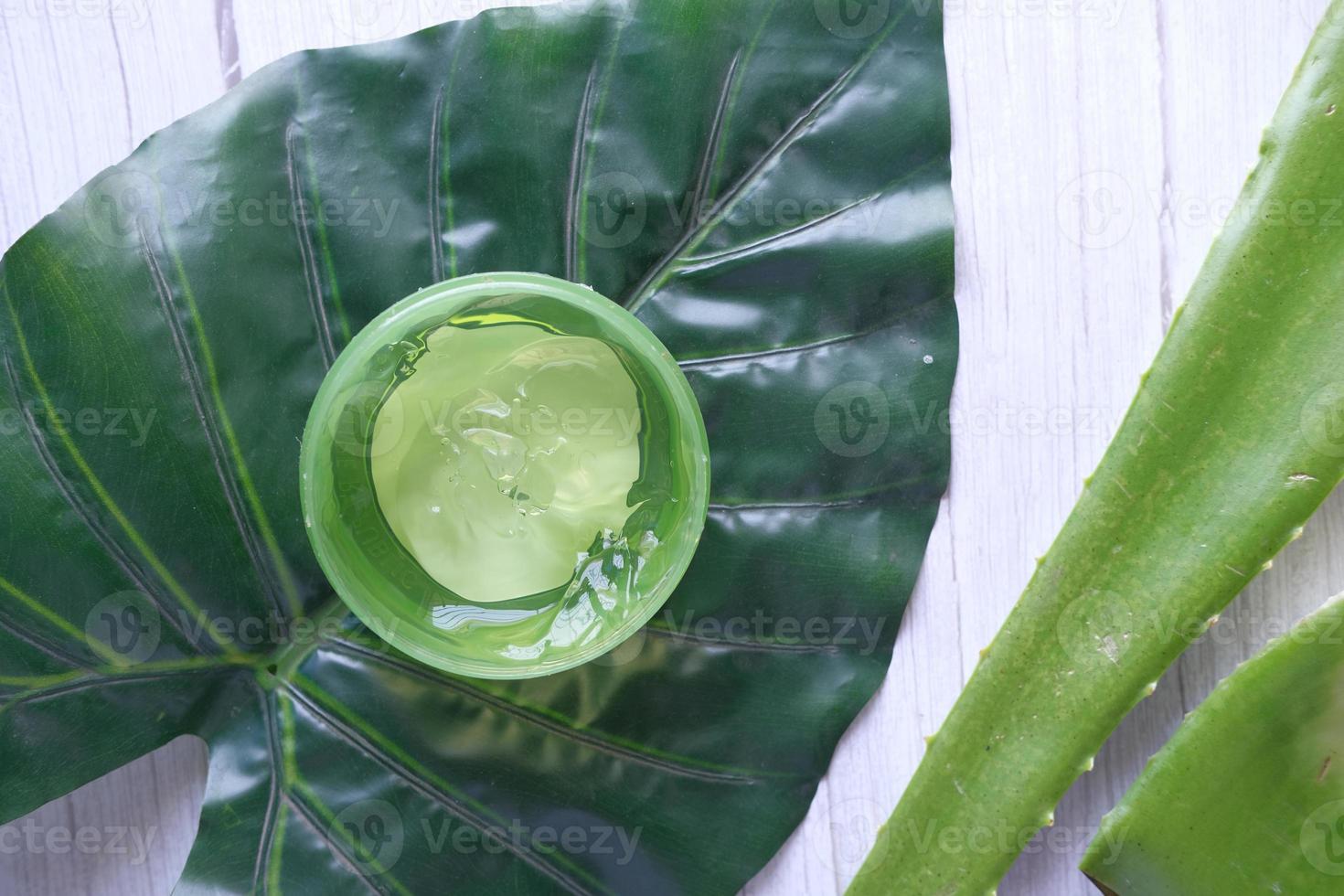 Aloe vera fresco fatiado e gel líquido em recipiente de plástico no fundo branco foto