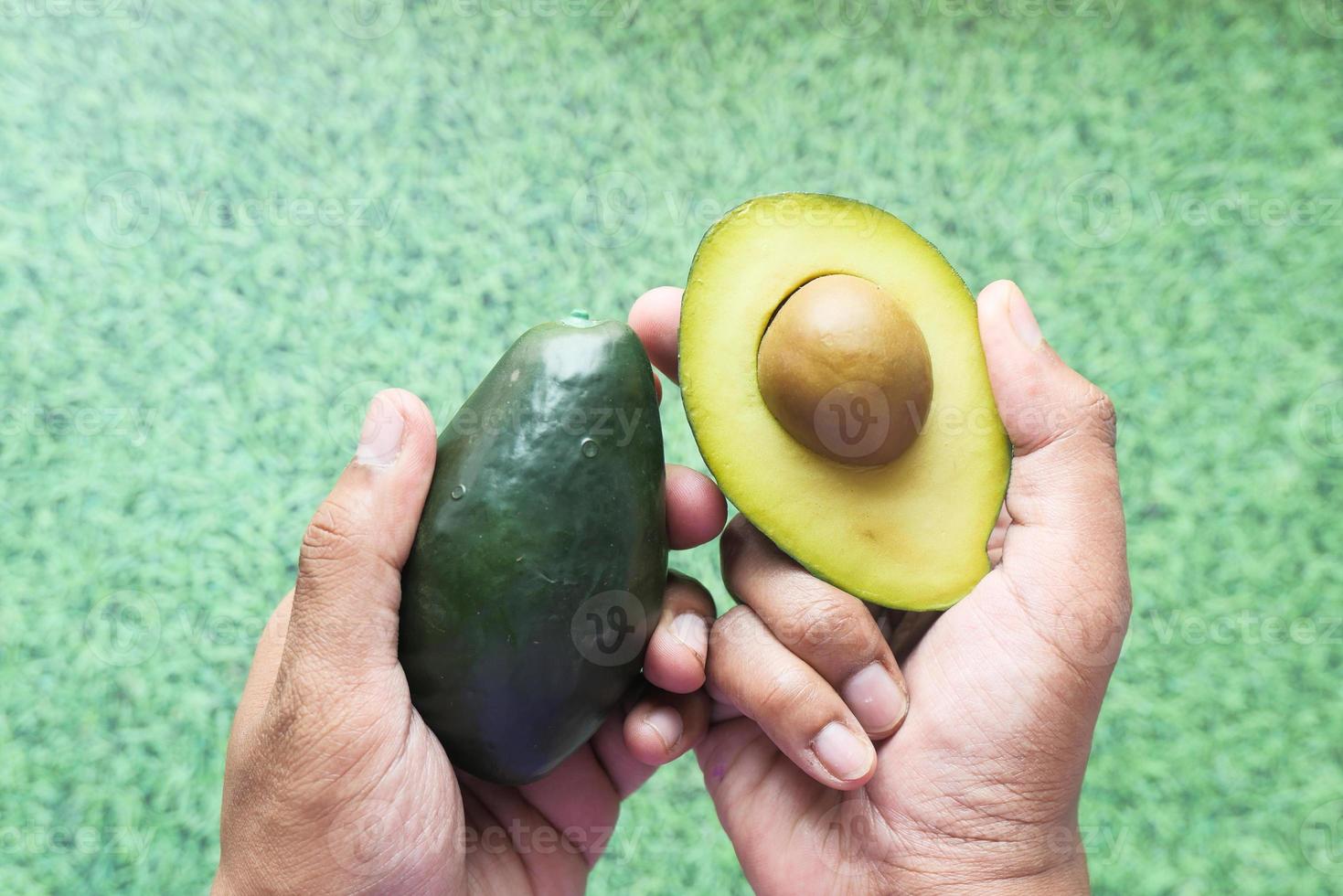 mão segurando uma fatia de abacate contra um fundo verde foto