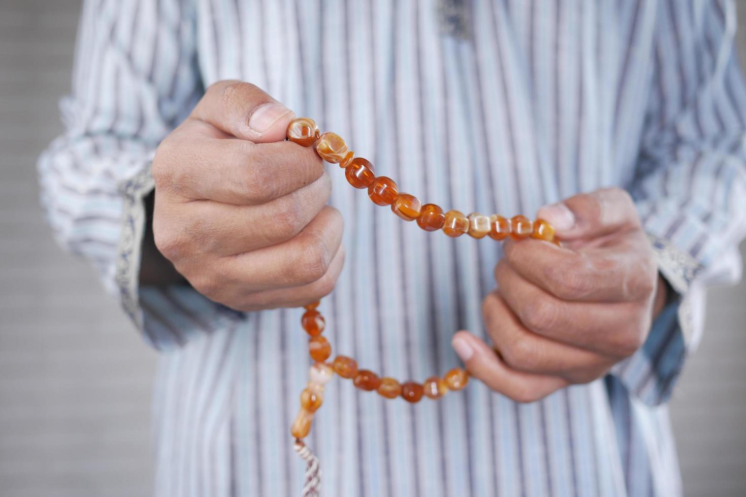 Feche a mão de um homem muçulmano com um rosário rezando no ramadã foto