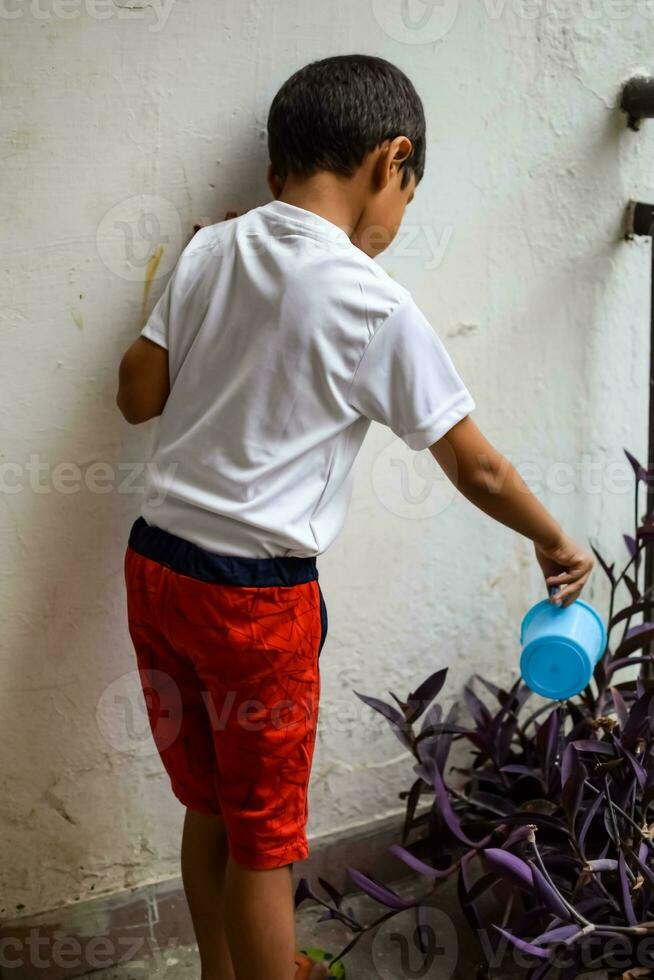 fofa 5 ano velho ásia pequeno Garoto é rega a plantar dentro a panelas localizado às casa sacada, amor do doce pequeno Garoto para a mãe natureza durante rega para dentro plantas, criança plantio foto