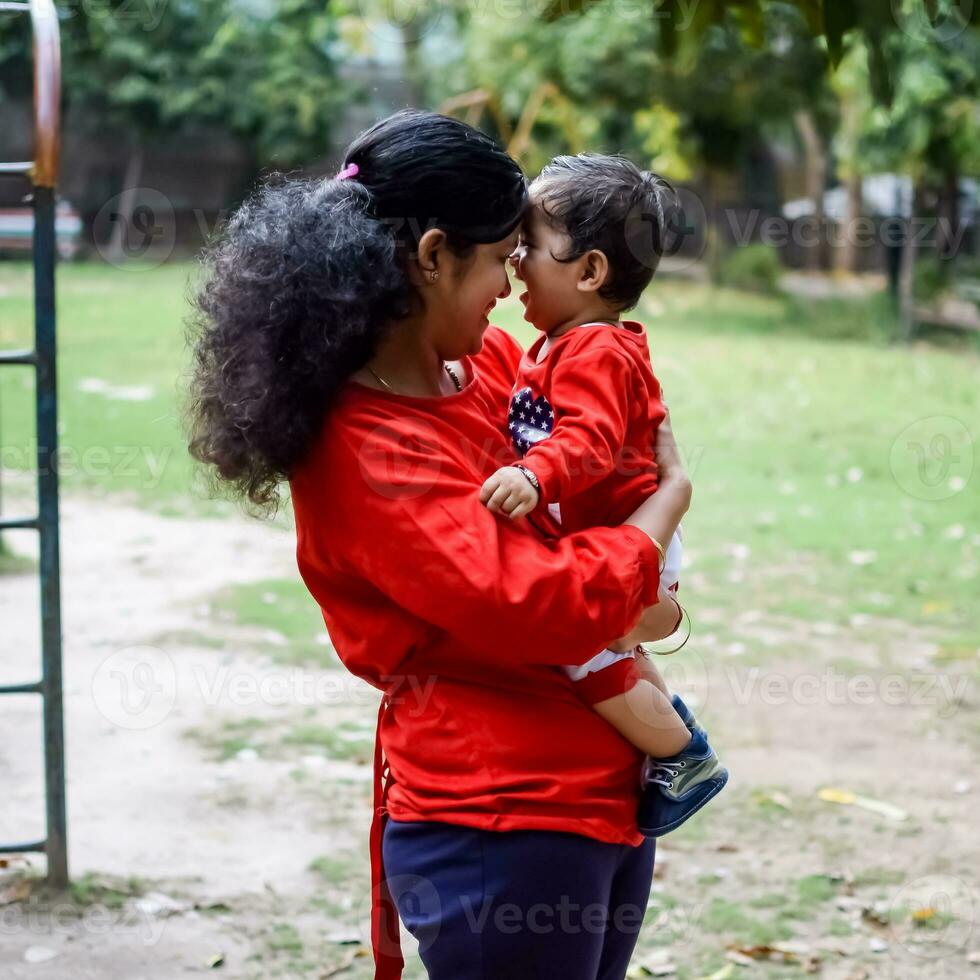 amoroso mãe carregando do dela bebê às sociedade parque. brilhante retrato do feliz mãe segurando criança dentro dela mãos. mãe abraçando dela pequeno 9 meses velho filho. foto