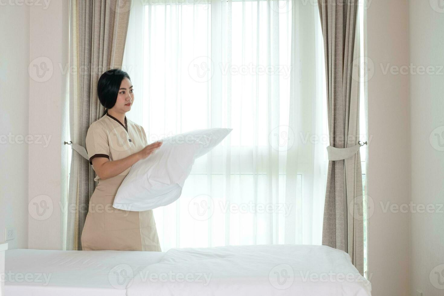 jovem bela empregada asiática organizando um travesseiro na cama em um quarto de hotel. foto