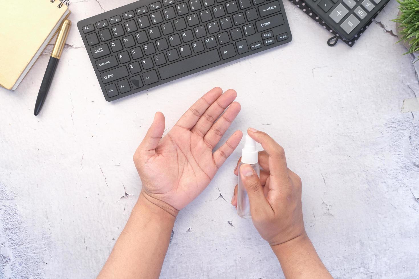 mão de jovem usando spray desinfetante para as mãos na mesa do escritório foto