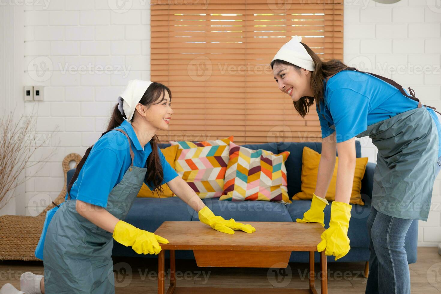 dois jovem mulheres dentro uniforme e luvas limpeza a vivo quarto às lar, elevação a mesa foto