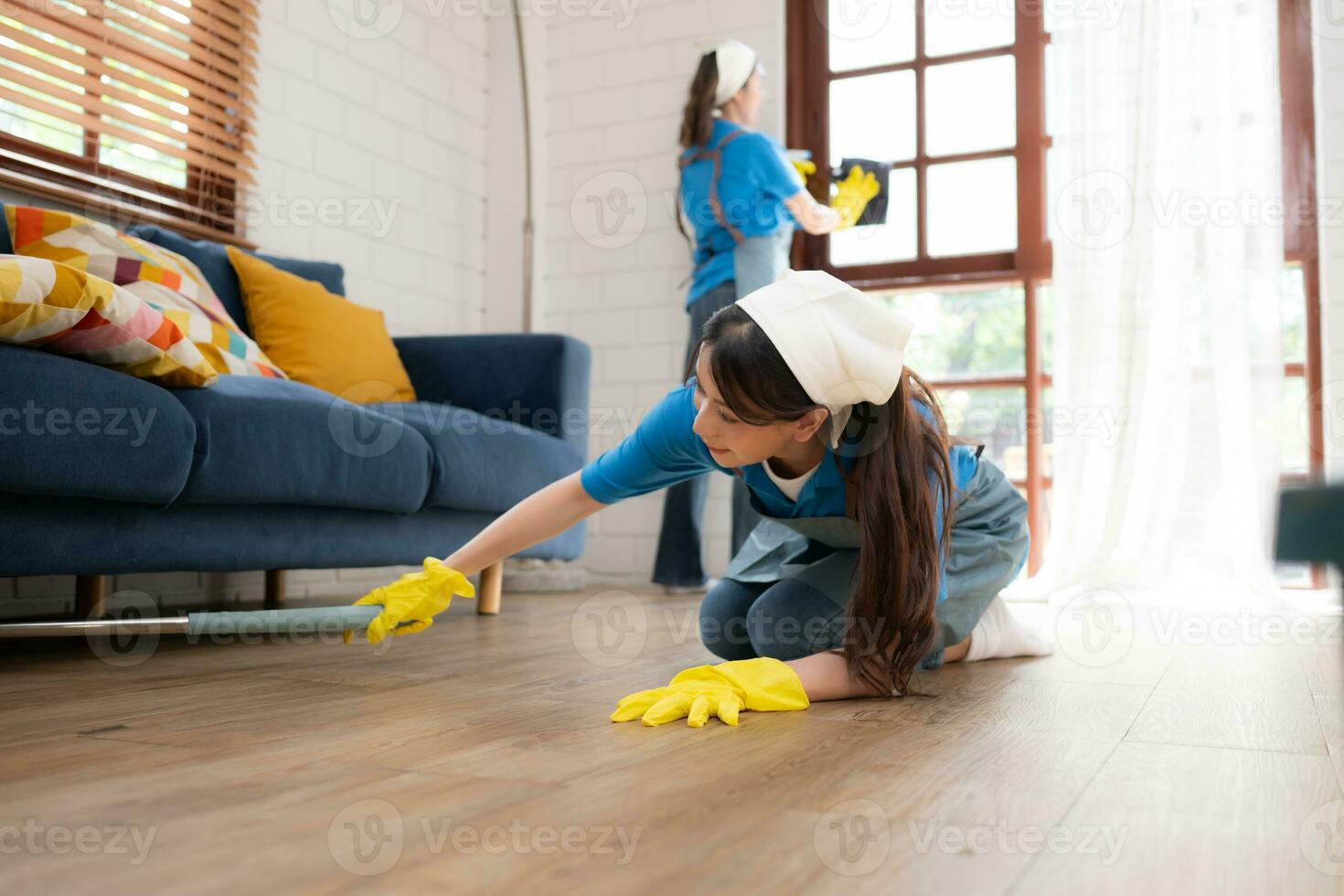 dois jovem mulheres dentro uniforme estão limpeza a vivo quarto às lar. foto