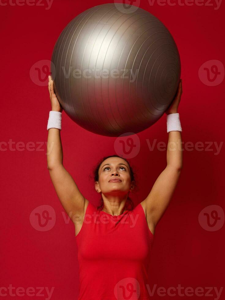 retrato do uma ginástica feliz em forma mulher em pé segurando uma em forma bola dentro dela elevado braços acima dela cabeça. cópia de livre espaço para texto. foto