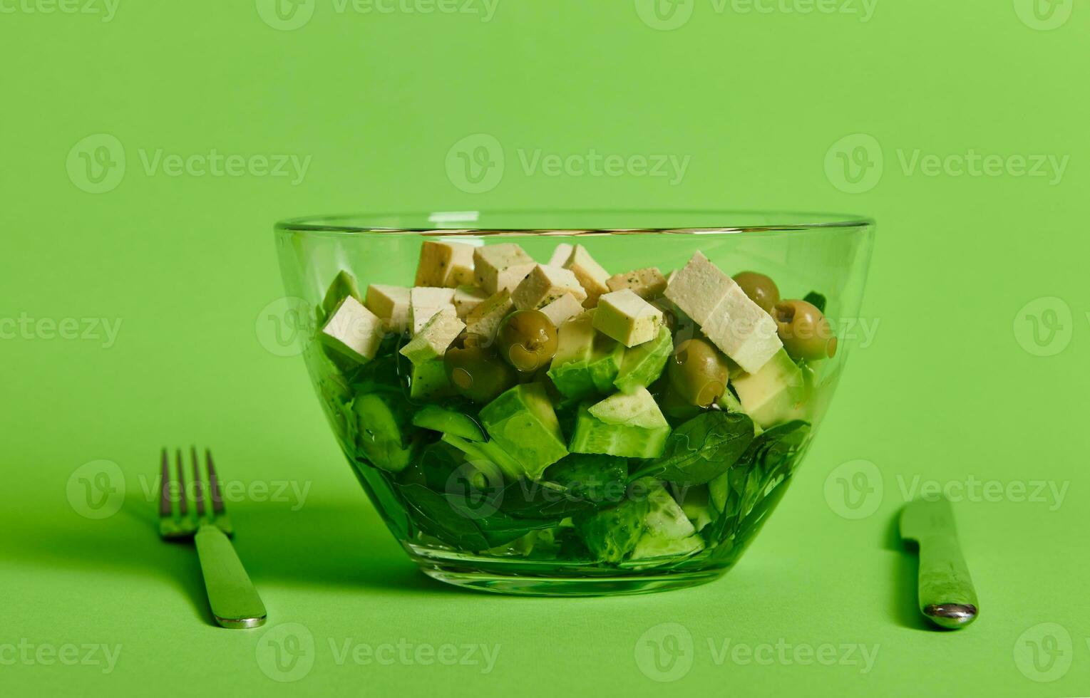 fechar-se do uma servindo tigela com verde salada e vegetais, e vegano tofu queijo em verde fundo foto