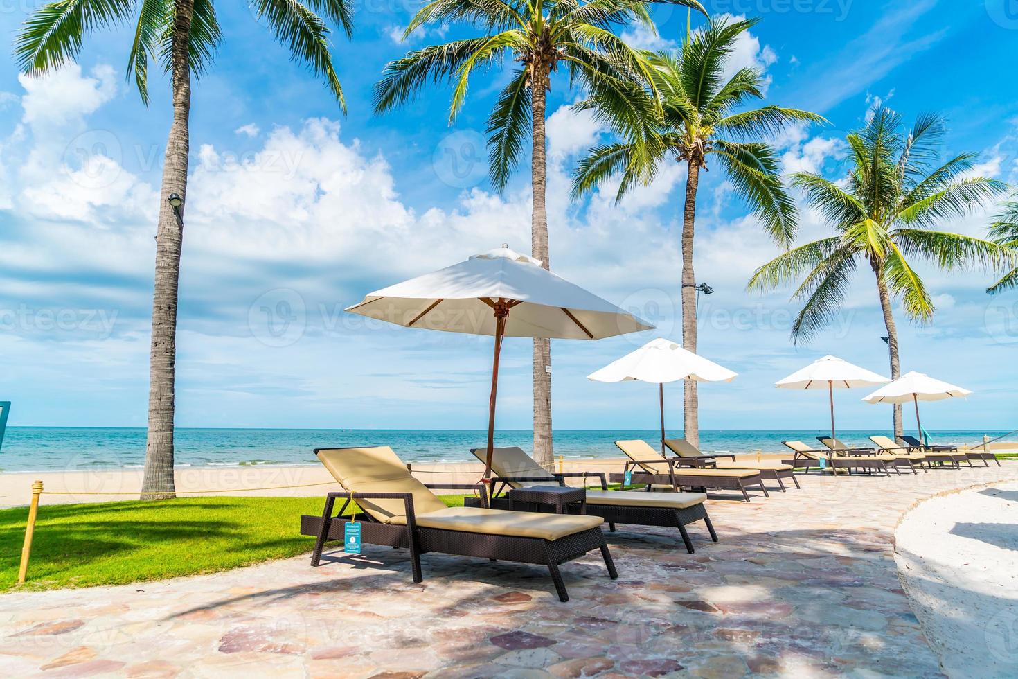 bela praia tropical e mar com guarda-sol e cadeira ao redor da piscina em hotel resort foto